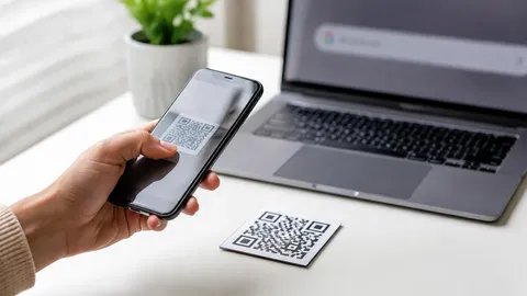 ภาพจำลองสมจริง: มือยกโทรศัพท์เหนือการ์ดลายโค้ดข้างแล็ปท็อปที่เปิดเบราว์เซอร์